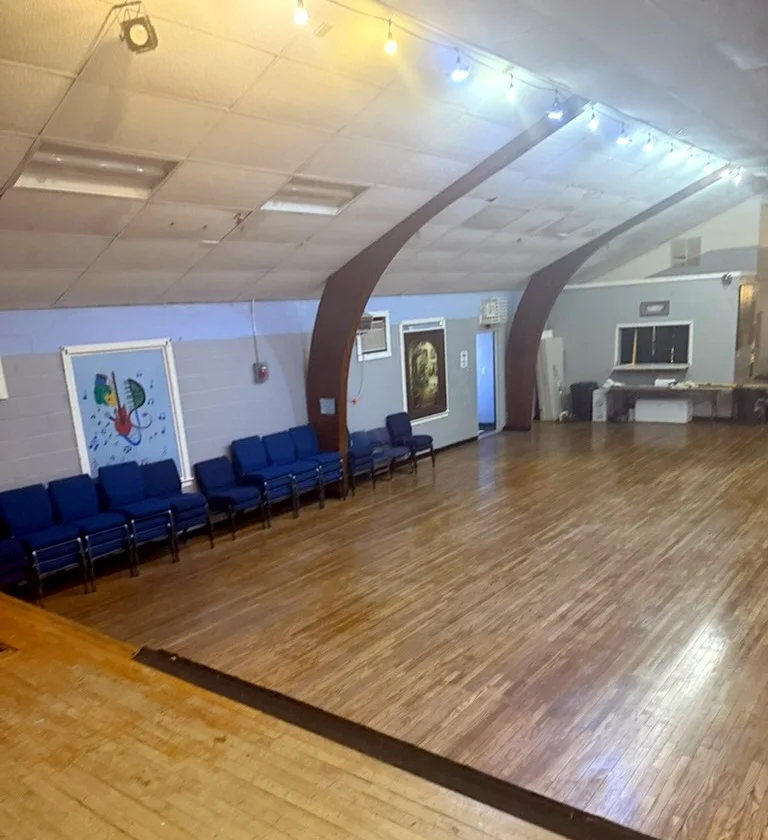 The main hall at IV THE YOUTH: a wood floor, blue chairs along the wall, and a painted mural of musical instruments.